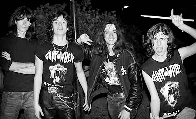 Cuatro jóvenes de Gunpowder posan de noche en blanco y negro con camisetas del grupo; uno levanta una baqueta.