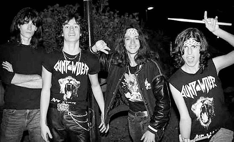 Cuatro jóvenes de Gunpowder posan de noche en blanco y negro con camisetas del grupo; uno levanta una baqueta.