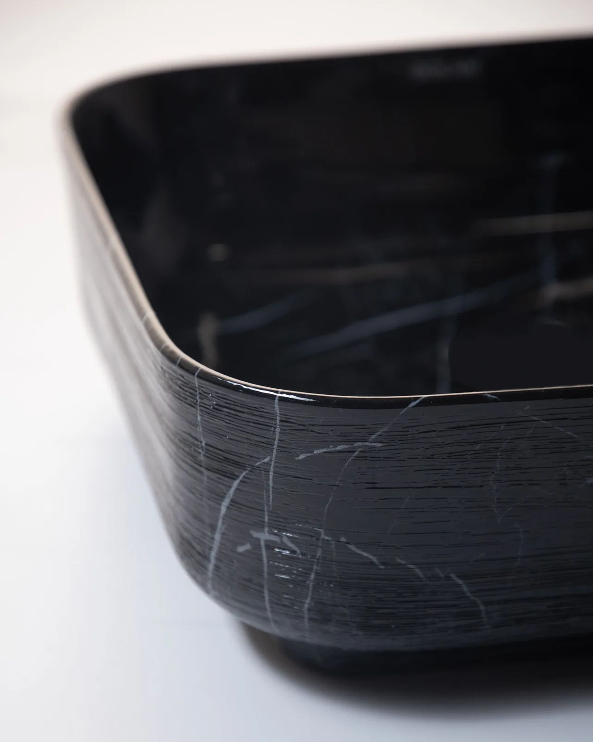 Detalle del borde de una bacha Bold negra veteada sobre una superficie blanca
