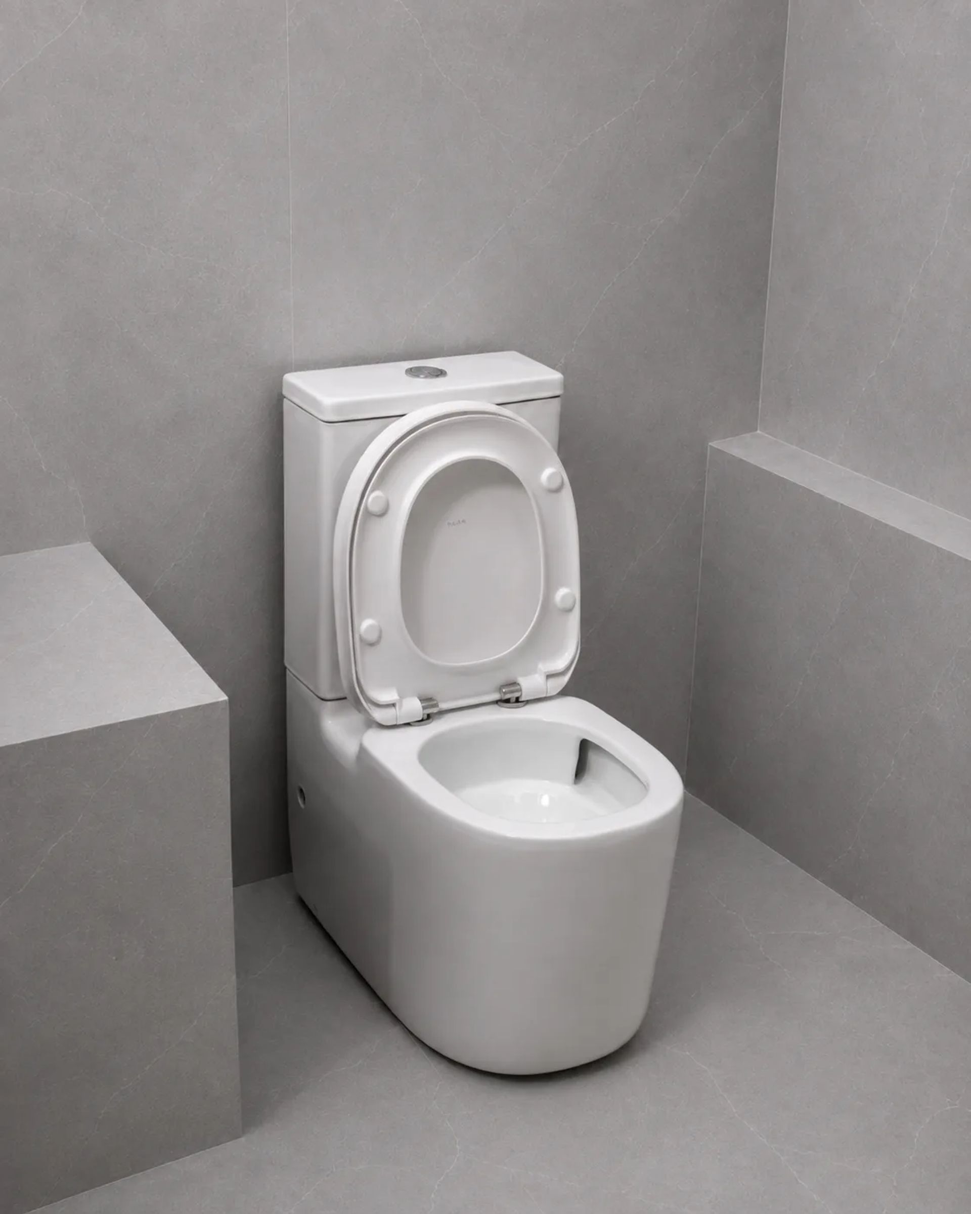 Inodoro Jade blanco con la tapa levantada, en un baño de paredes y piso grises