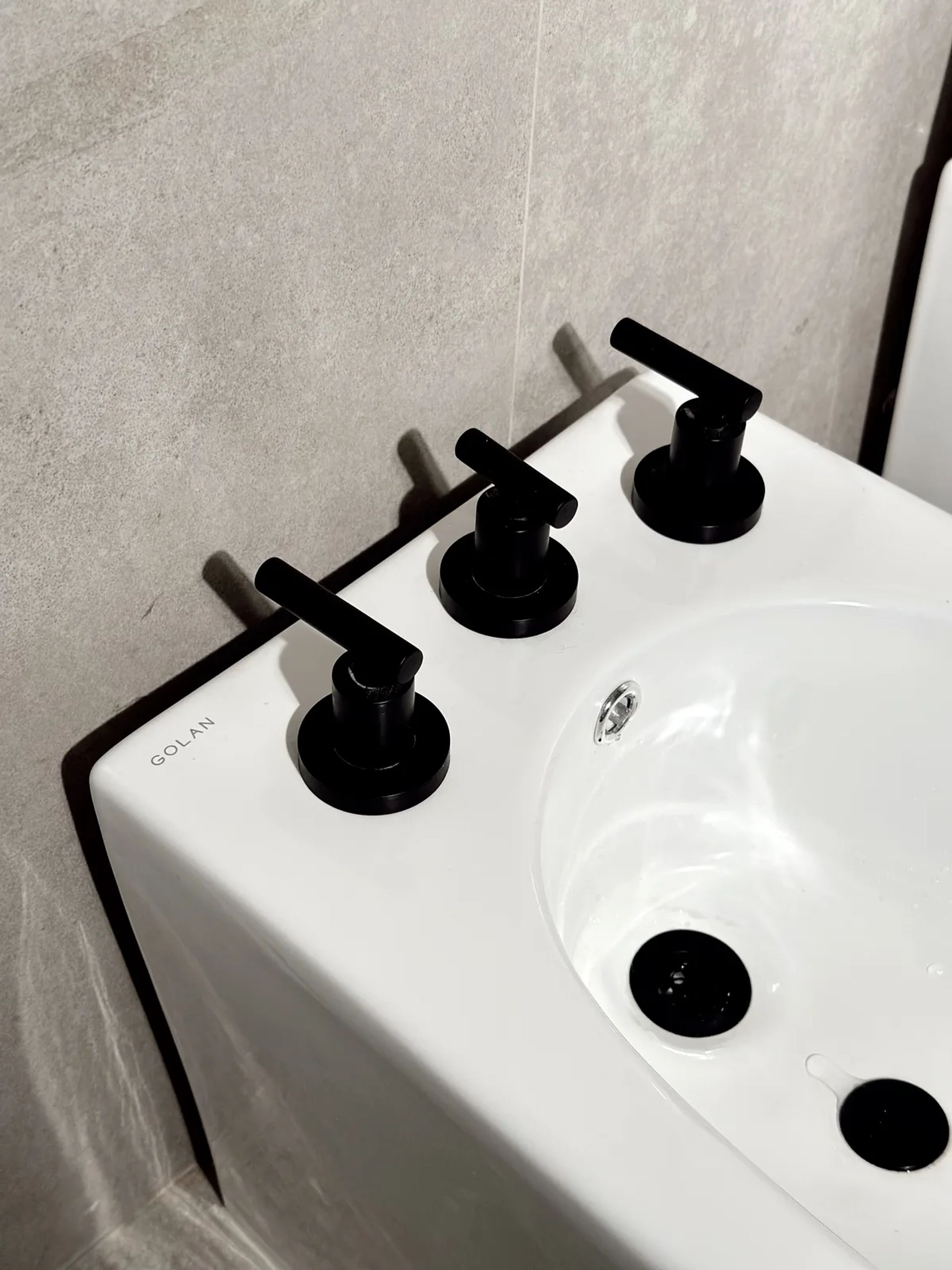 Bidet blanco con grifería negra de tres llaves, de cerca