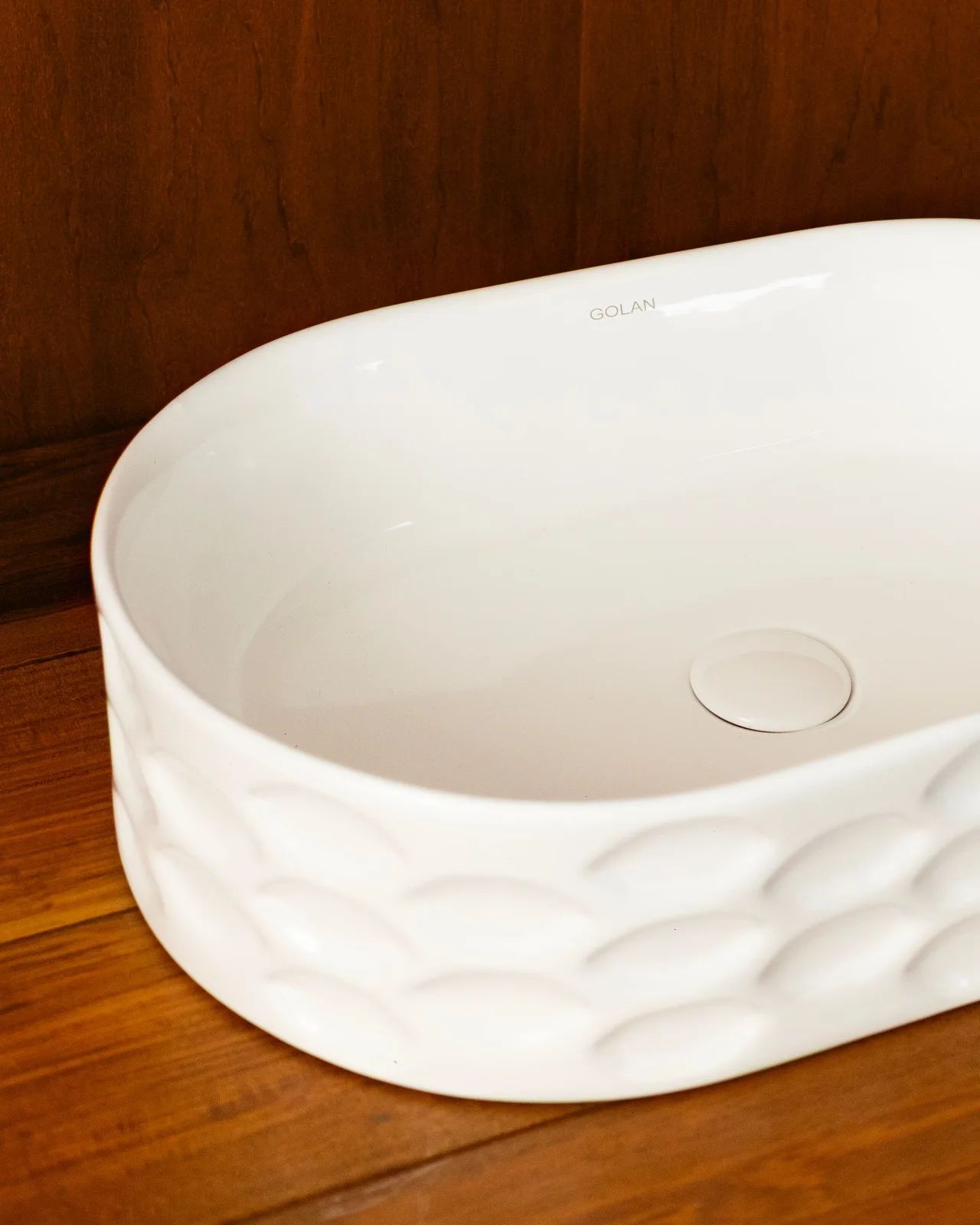 Bacha de apoyo Nova blanca, ovalada y con relieve, sobre una mesada de madera