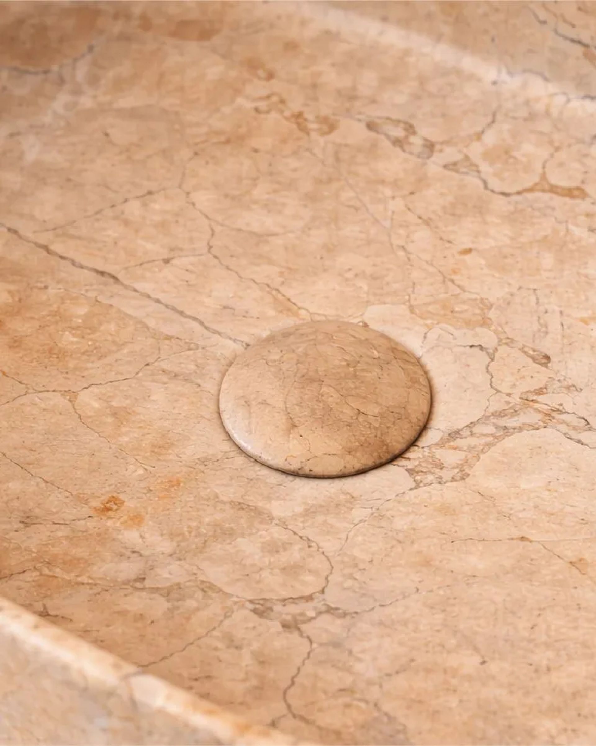 Detalle del interior de una bacha Terra de piedra beige veteada, con su tapa de desagüe