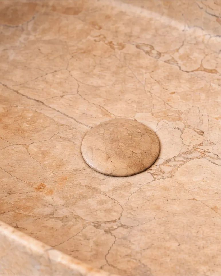 Detalle del interior de una bacha Terra de piedra beige veteada, con su tapa de desagüe
