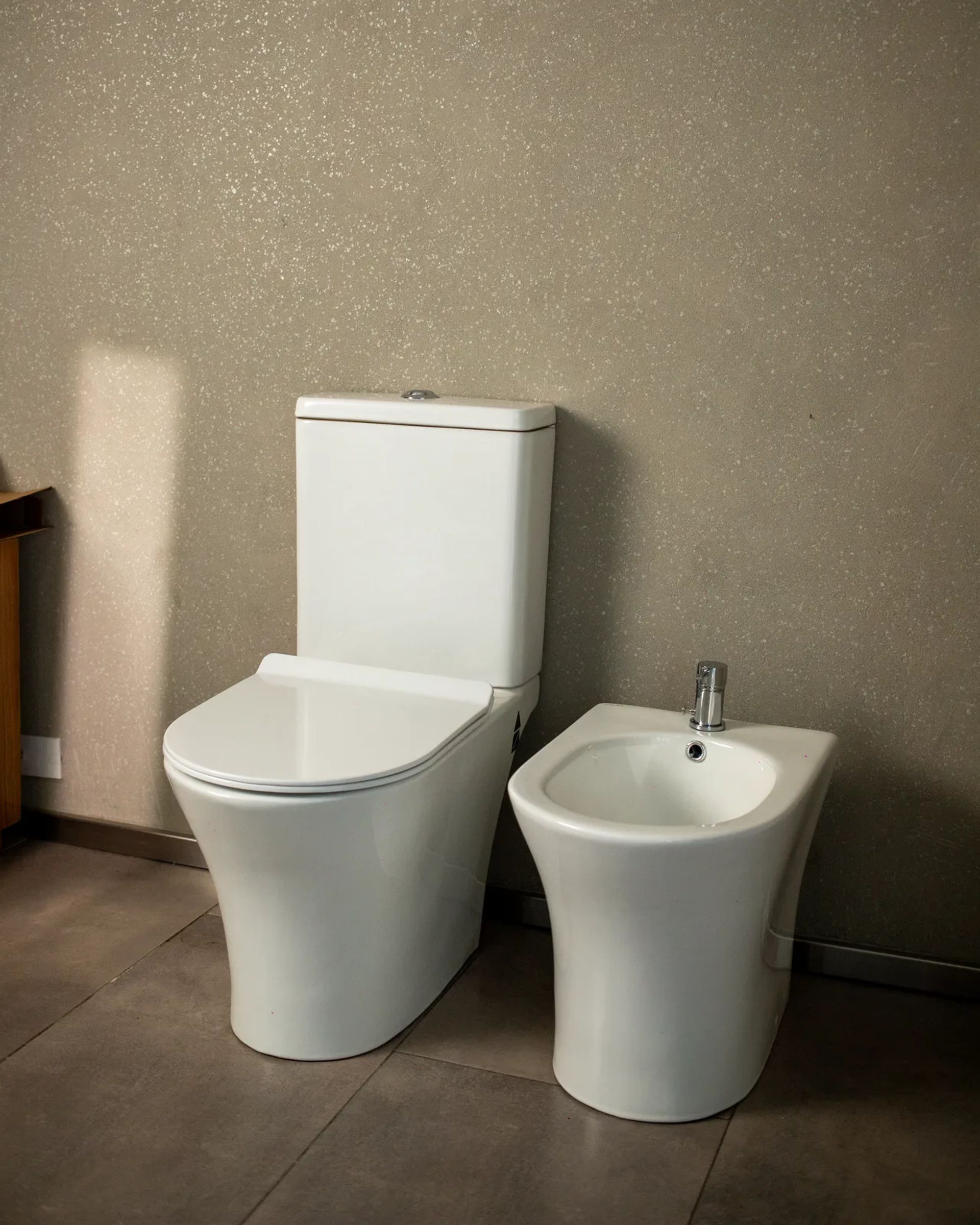 Inodoro y bidet Symphony blancos en un baño de paredes cálidas, con luz de ventana