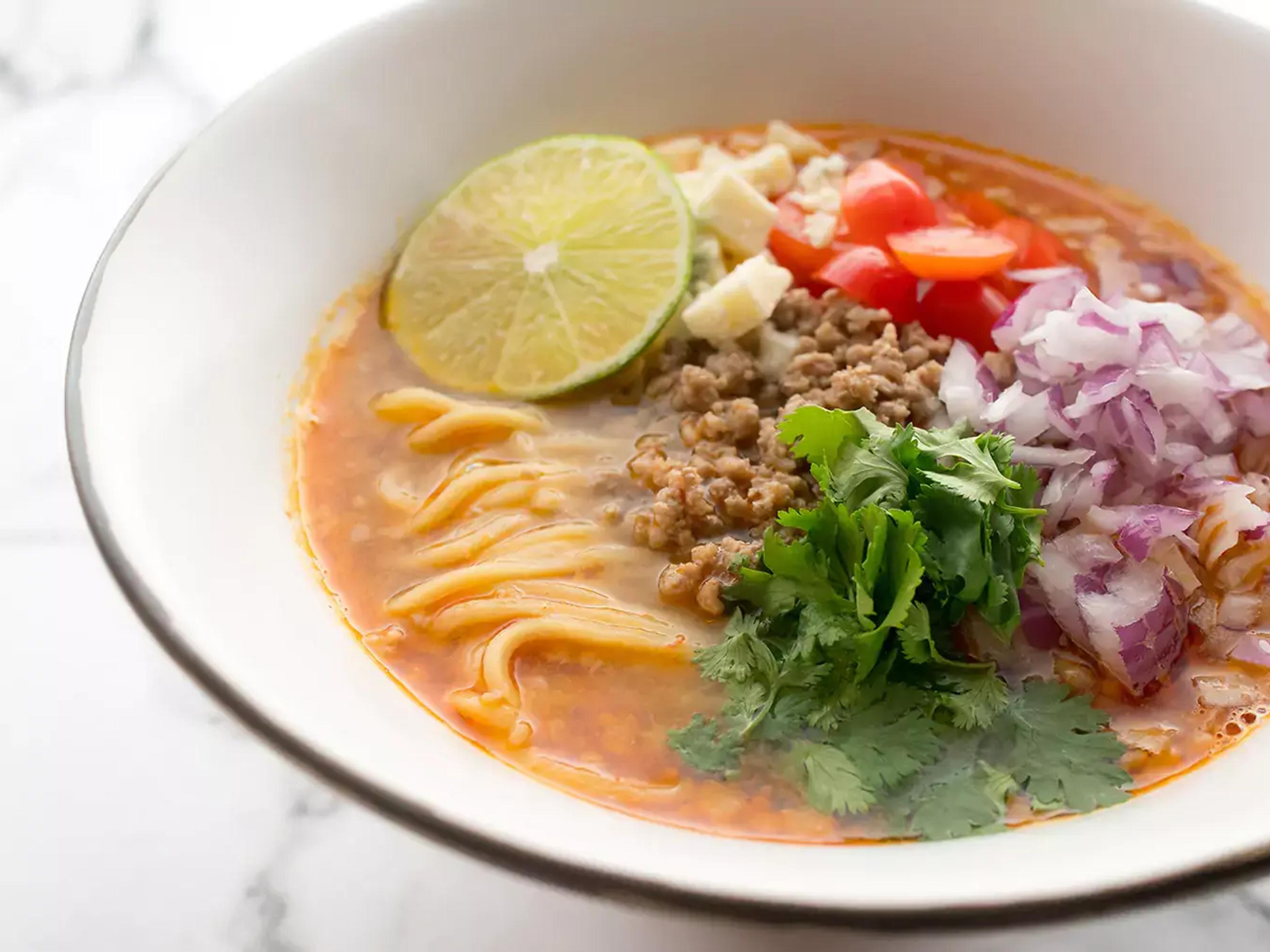 A bowl of ramen with a slice of lime, cilantro, pepper, red onion and garlic as toppings.