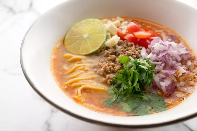 A bowl of ramen with a slice of lime, cilantro, pepper, red onion and garlic as toppings.