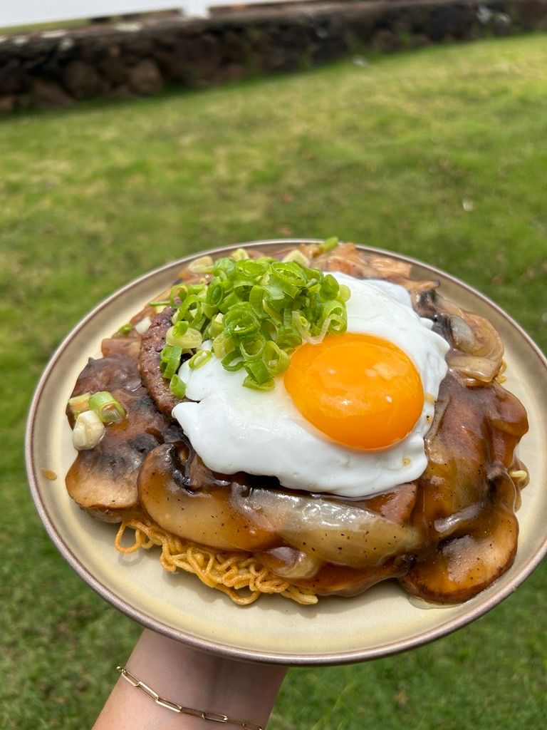 A plate of Cake Noodle topped with a hamburger patty, egg, gravy, and green onion.