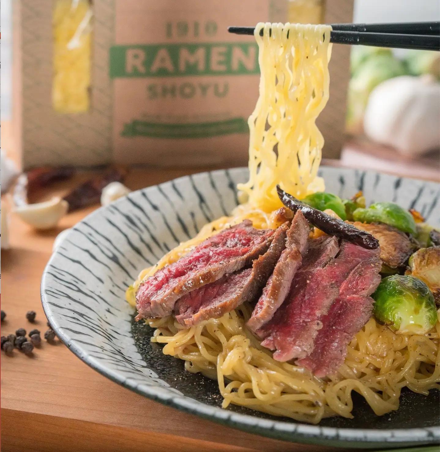 Side image of a plate with Shoyo beef ramen pasta and chopsticks holding some of the ramen