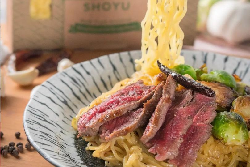 Side image of a plate with Shoyo beef ramen pasta and chopsticks holding some of the ramen