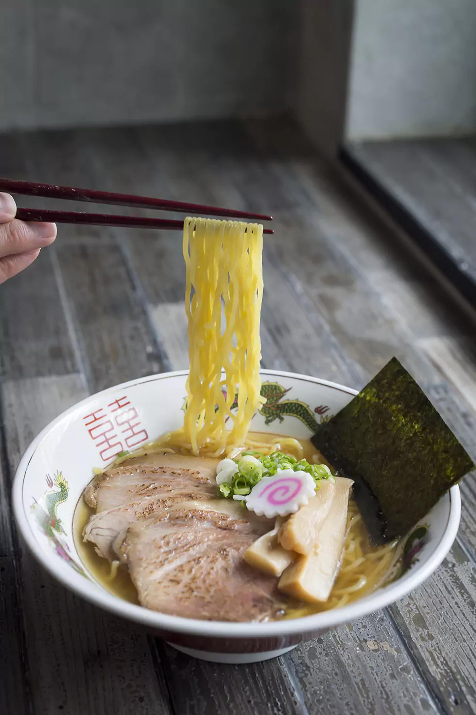 shoyu ramen on a bowl with noodles being pulled with chopsticks.