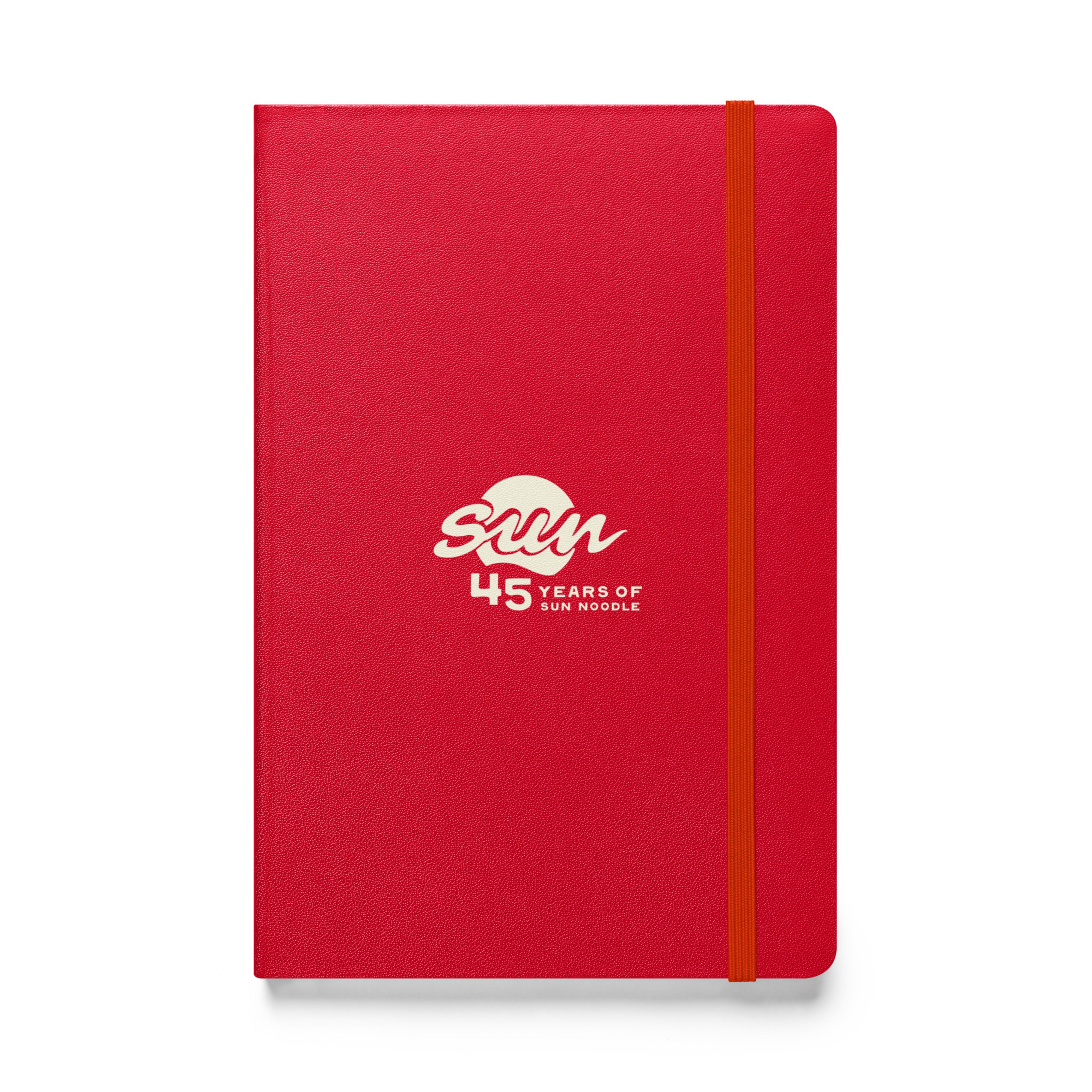 Red hardcover bound notebook with an orange elastic closure band, featuring the cream "45 Years of Sun Noodle" logo centered on the cover, with a stylized "sun" script over a circle.
