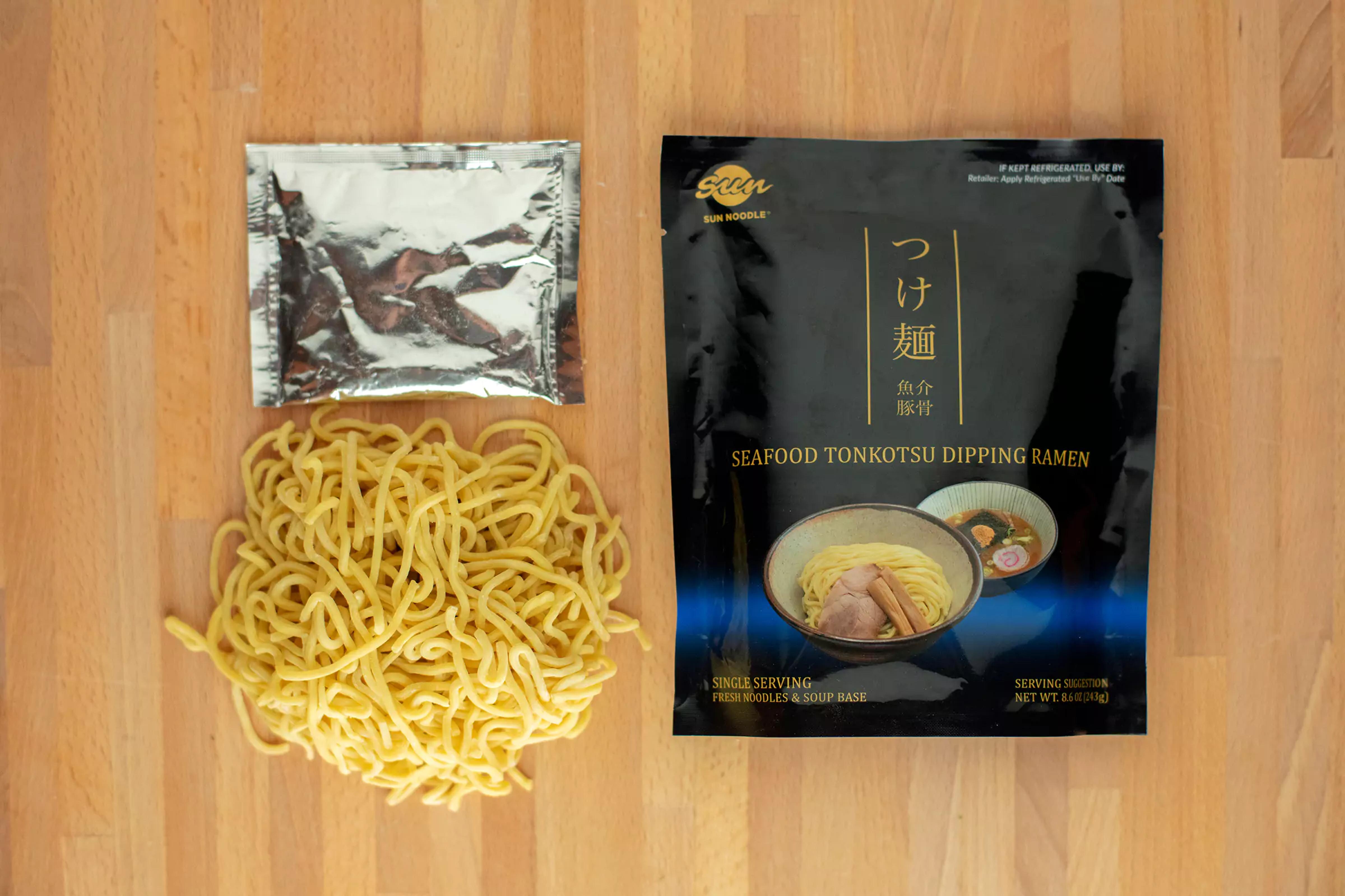 Top videw with Seafood tonkotsu dipping ramen product laying on table with noodles and broth packaging next to it.