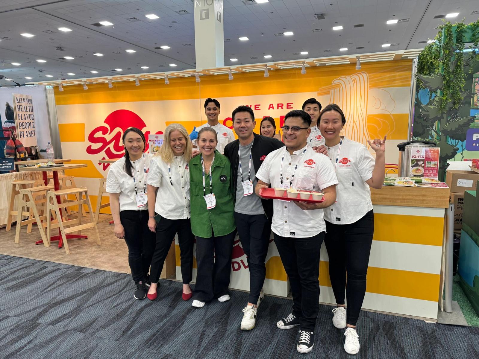 Sun Noodle team at their booth in Expowest 2024 with someone holding testers