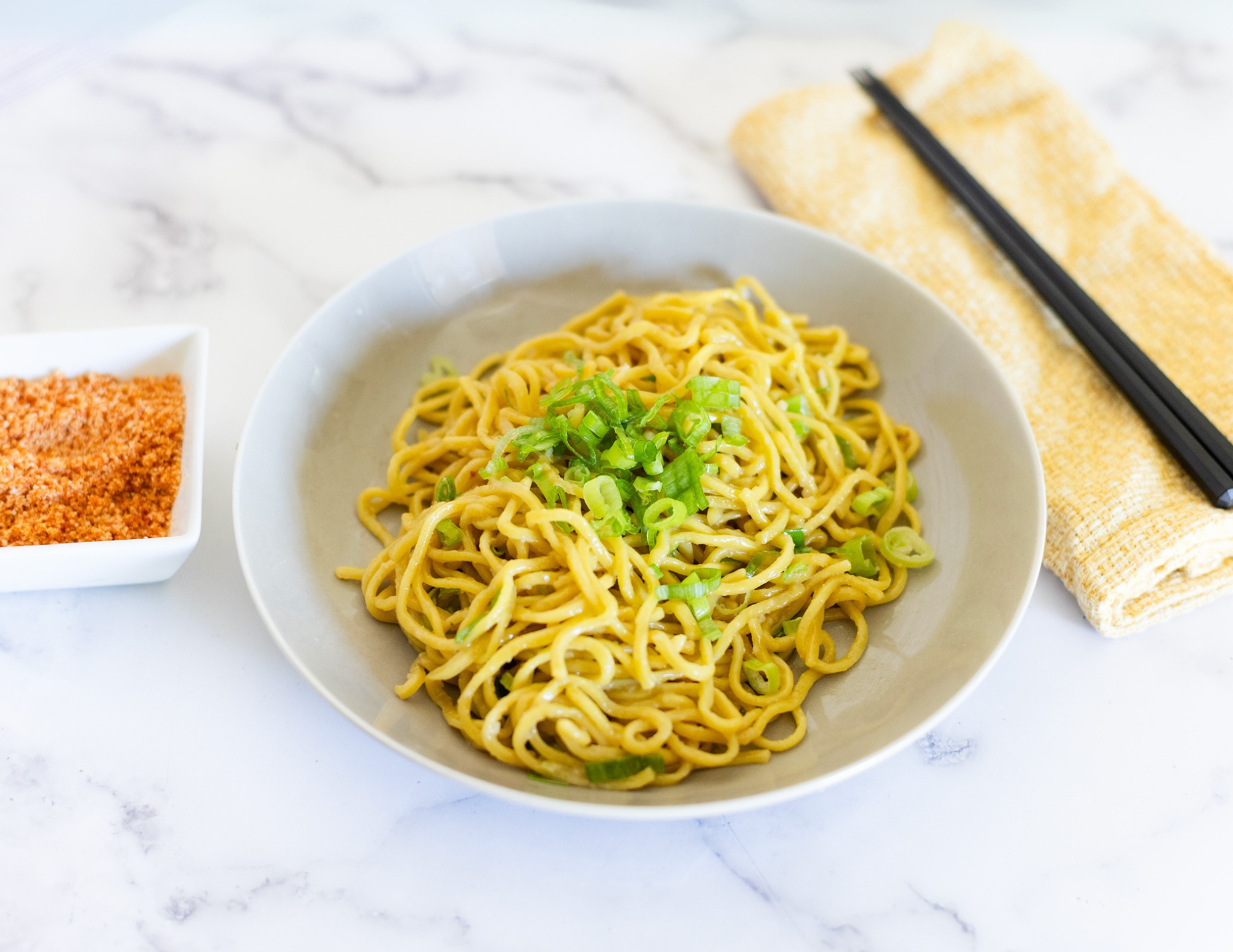 An image of a table setting with garlic noodles, chopsticks, and seasoning.