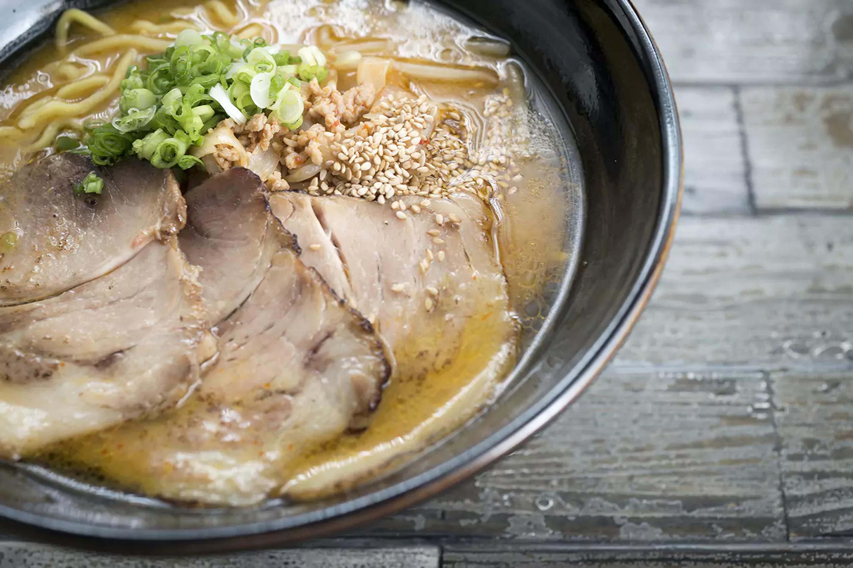 Cooked miso ramen kit on a bowl with meat and garnished with sesame and chives.