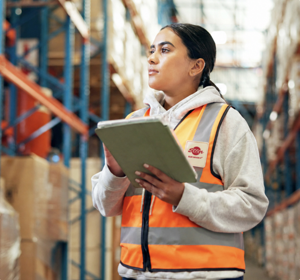 Warehouse worker in a Sun Noodle safety vest checking a tablet