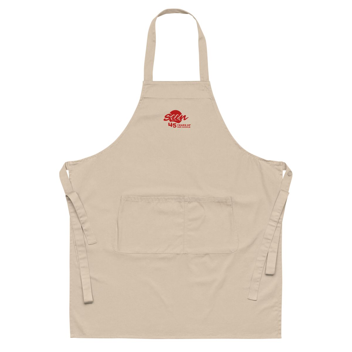 Beige organic cotton apron with a neck loop, waist ties, and a front pocket, embroidered near the chest with the red "45 Years of Sun Noodle" logo featuring a stylized "sun" script over a red circle.