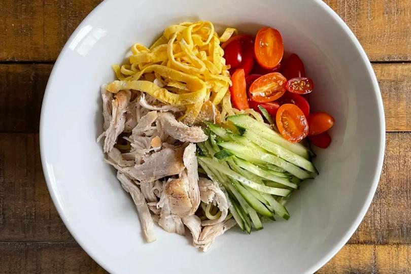 Top view of food plate with ramen, tomatoes, steamed chicken, and cucubers