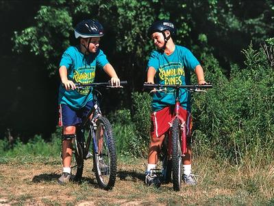 two campers riding bikes together wearing helmets and Rambling Pines Day Camp t-shirts