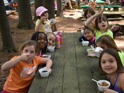 kids sitting around a picnic table eating and smiling at the camera at Rambling Pines Day Camp