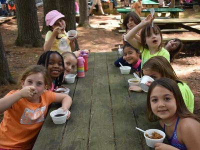 kids sitting around a picnic table eating and smiling at the camera at Rambling Pines Day Camp