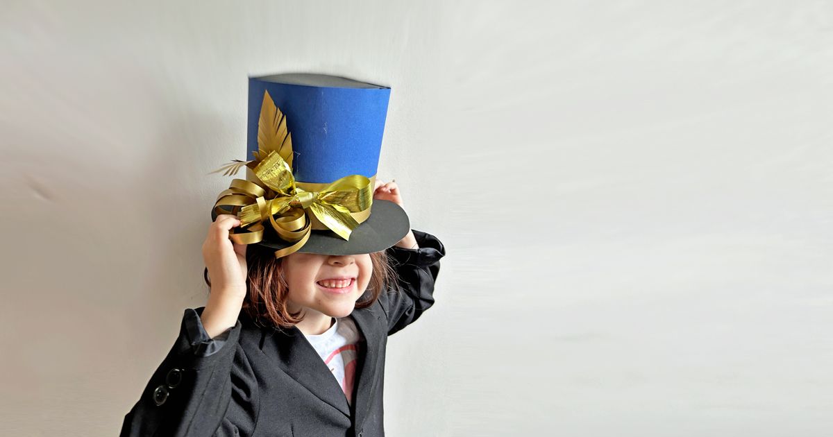 A grinning child wears a paper tophat decorated with gold trimming
