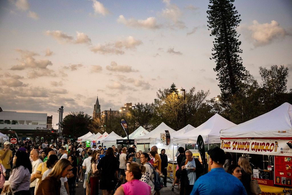 The busy Randwick Creative Night market at twilight, with people browsing a row of food stalls.