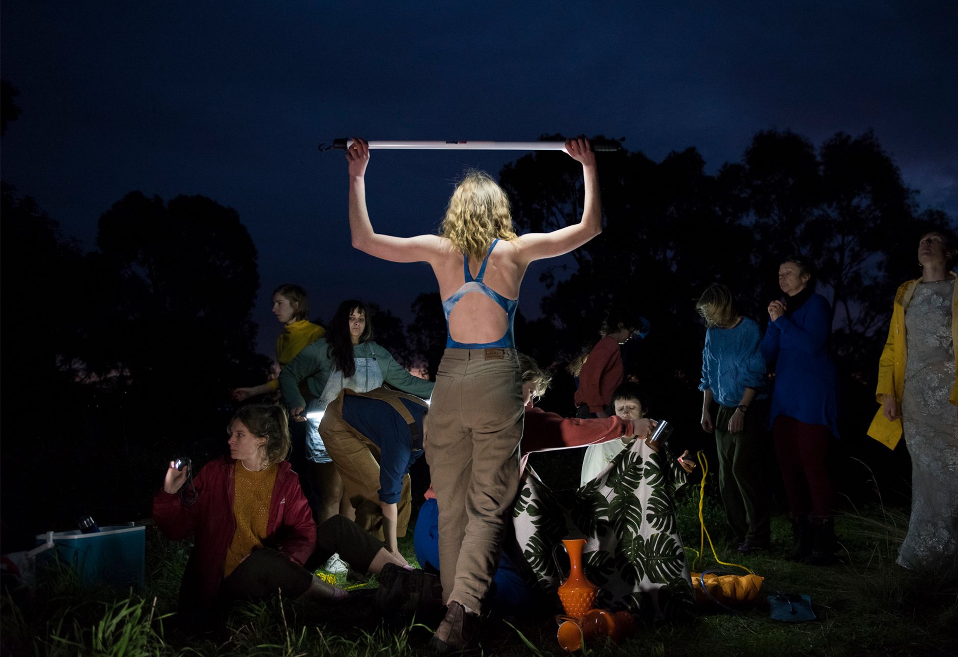 A Deep Soulful Sweats performer stands spotlit in the centre of a darkened stage, holding a bar above her head