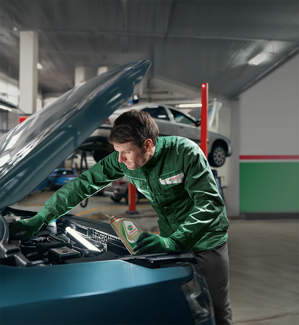 Mekaniker i Castrol Service-jakke der tjekker under motorhjelmen på en bil, mens han holder en flaske Castrol Edge-olie