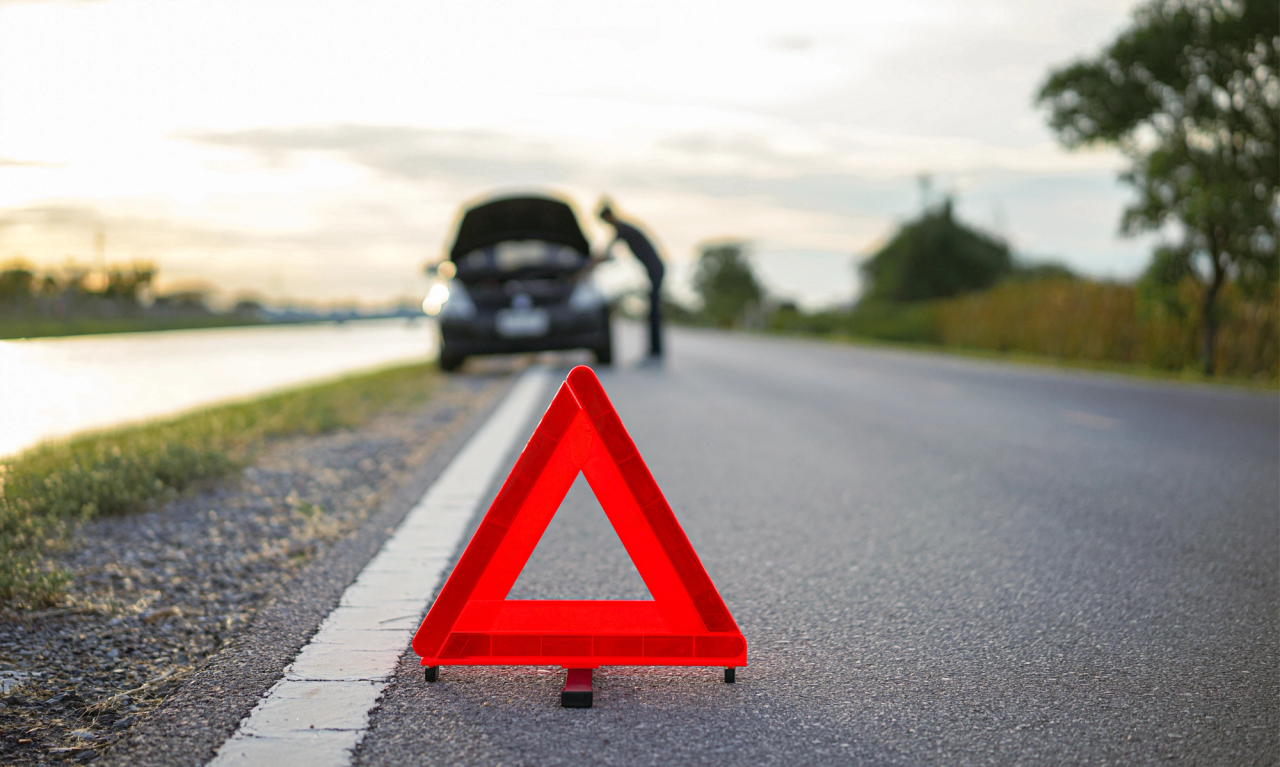 Rødt advarselstrekant ved vejkanten foran en bil med åben motorhjelm, hvor en person tjekker motoren.