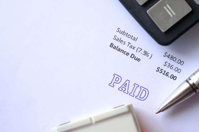 Close-up of an invoice stamped "PAID" showing subtotal, sales tax, and balance due, with a pen and calculator resting on top.