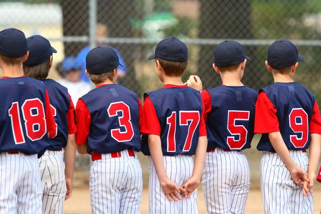 photo of a little league baseball team in their uniforms standing in line with the backs to the photographer