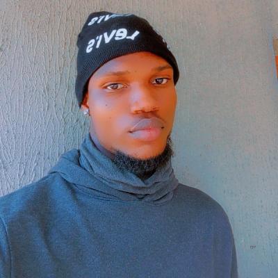 <A man with a short goatee, black beanie, and earrings looks forwards in front of a plain background.>