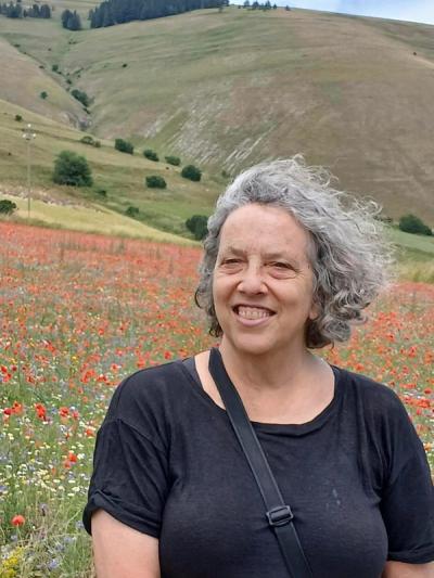 A photo of Jacqueline Oshervow smiling in a field of red flowers. 