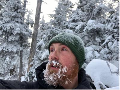 A photo of Josh Nicolaisen with icicles in their beard.  
