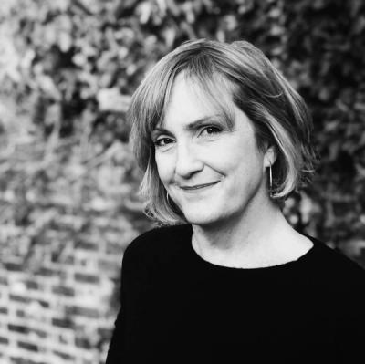 <A black and white picture of a woman with short blonde hair standing in front of a brick wall>