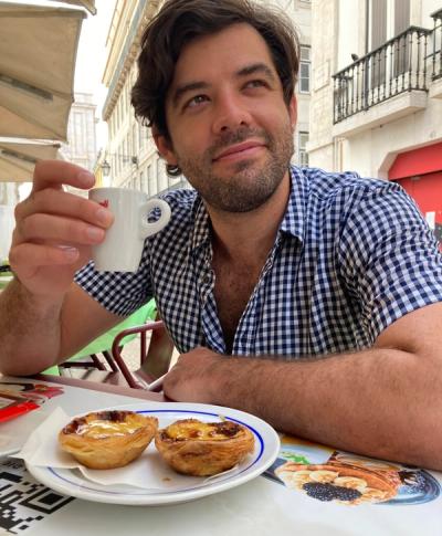 Photo of Lucian Mattison holding an espresso cup and wearing a blue plaid shirt. 