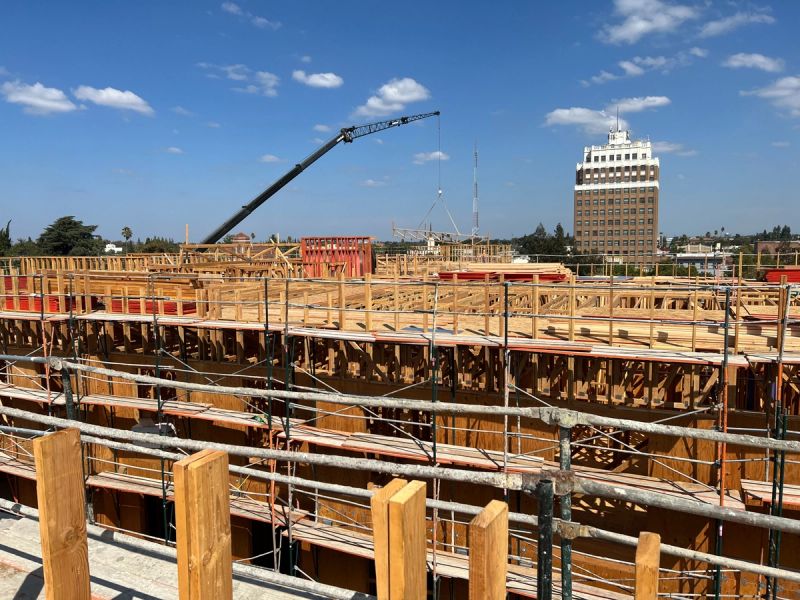 Boom crane setting commercial roof trusses on a large-scale building frame with scaffolding and downtown Sacramento skyline visible in the background by Mike Walker Lumber Co Inc