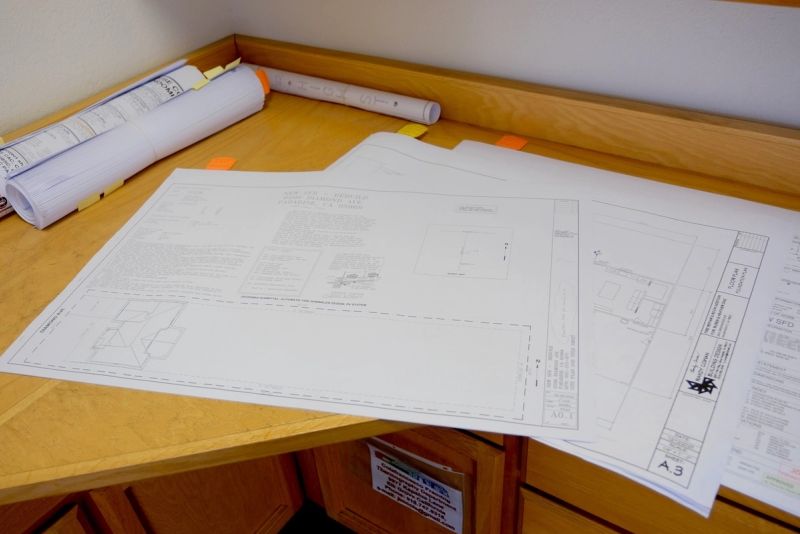 Stamped truss engineering drawings and architectural blueprints spread out on a desk at the Mike Walker Lumber Co Inc office during a design consultation review