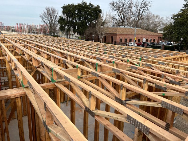 Rows of open-web engineered floor trusses with steel connector plates and green bracing straps installed on a commercial building in Sacramento by Mike Walker Lumber Co Inc