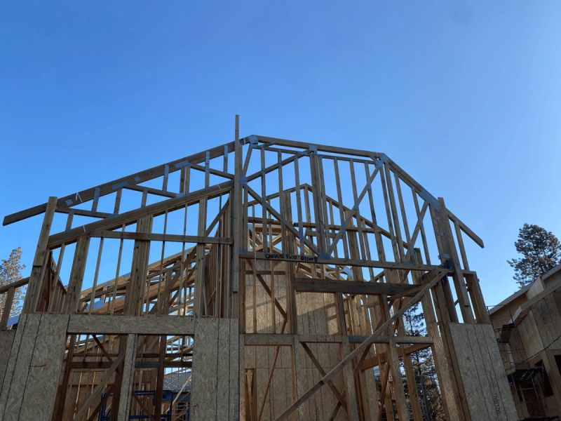 Custom residential roof trusses framed on a new home addition showing gable and hip truss connections against a clear blue sky by Mike Walker Lumber Co Inc