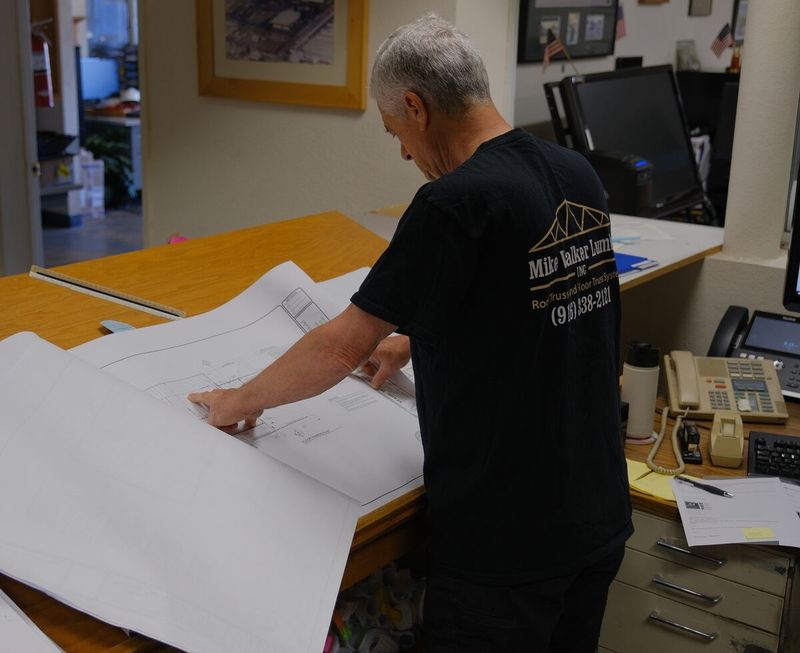 Mike Walker Lumber Co Inc engineer reviewing architectural blueprints and truss design plans at the drafting table during a project consultation