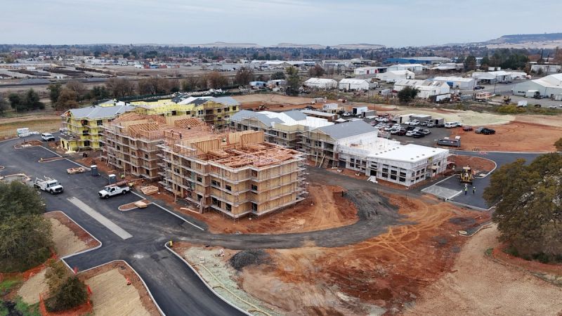 Aerial view of a multi-family apartment complex under construction with wood-framed buildings and engineered roof trusses at various stages of completion by Mike Walker Lumber Co Inc