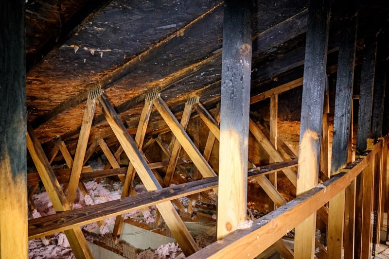 Fire-damaged roof trusses inside an attic showing charred lumber and new replacement truss members being installed for structural restoration by Mike Walker Lumber Co Inc