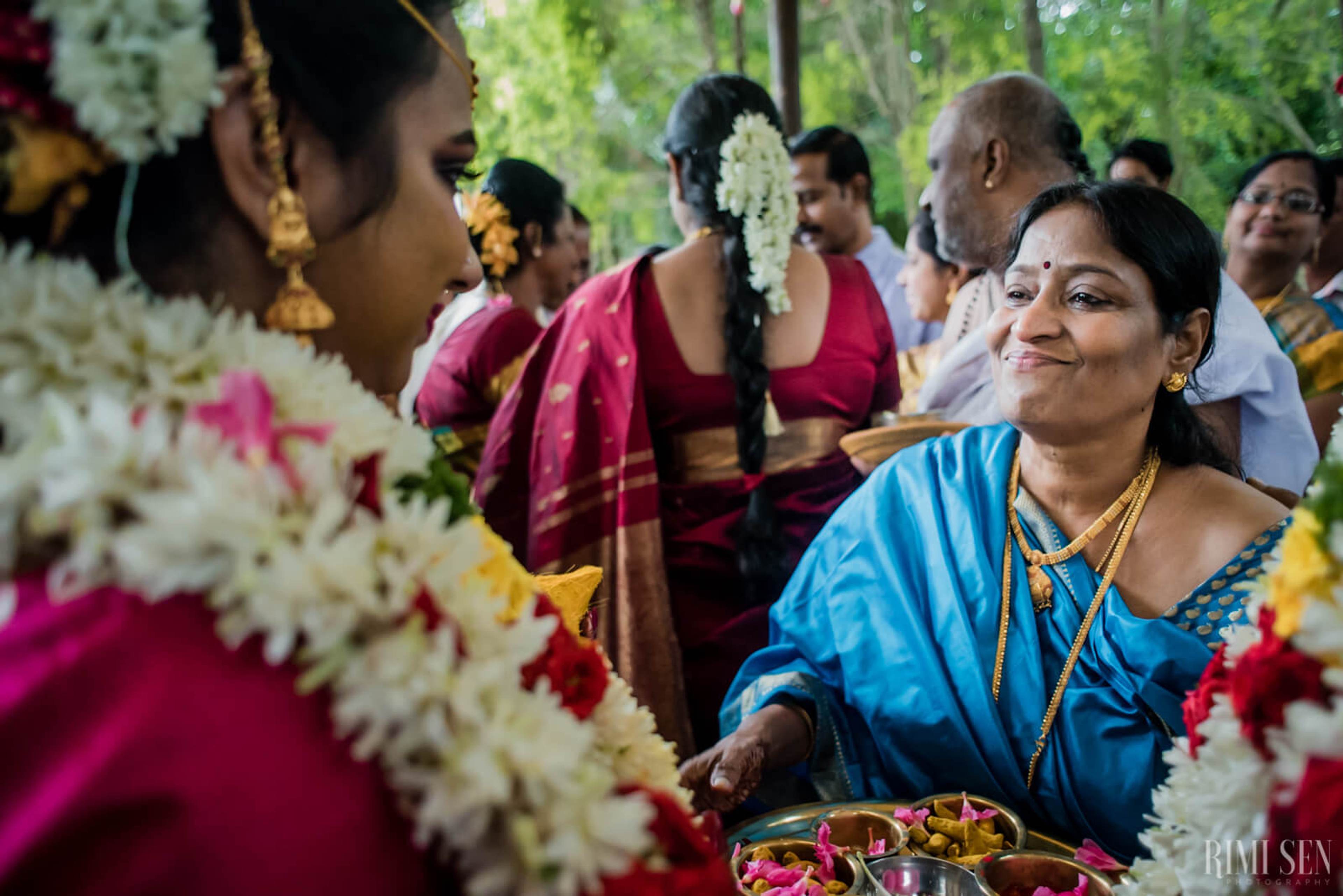 Woman in blue silk saree smiling at ceremony with white flower garlands and guests in Bangalore wedding celebration