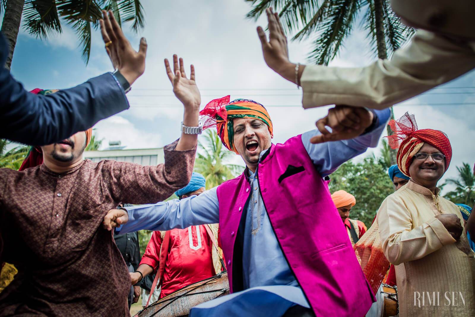 Pooja and Aniket celebrate with joyful guests in colorful traditional attire under palm trees in Bangalore