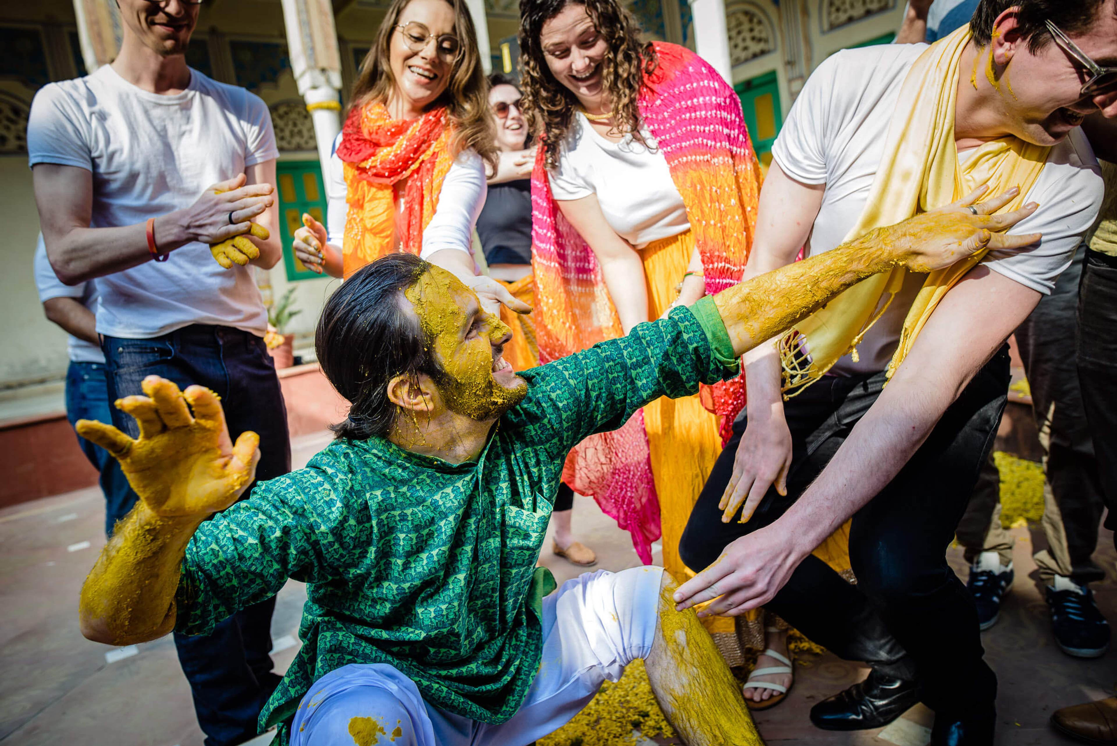 Maitrayee and Eric covered in yellow powder, celebrating with guests during Holi festival in Rajasthan