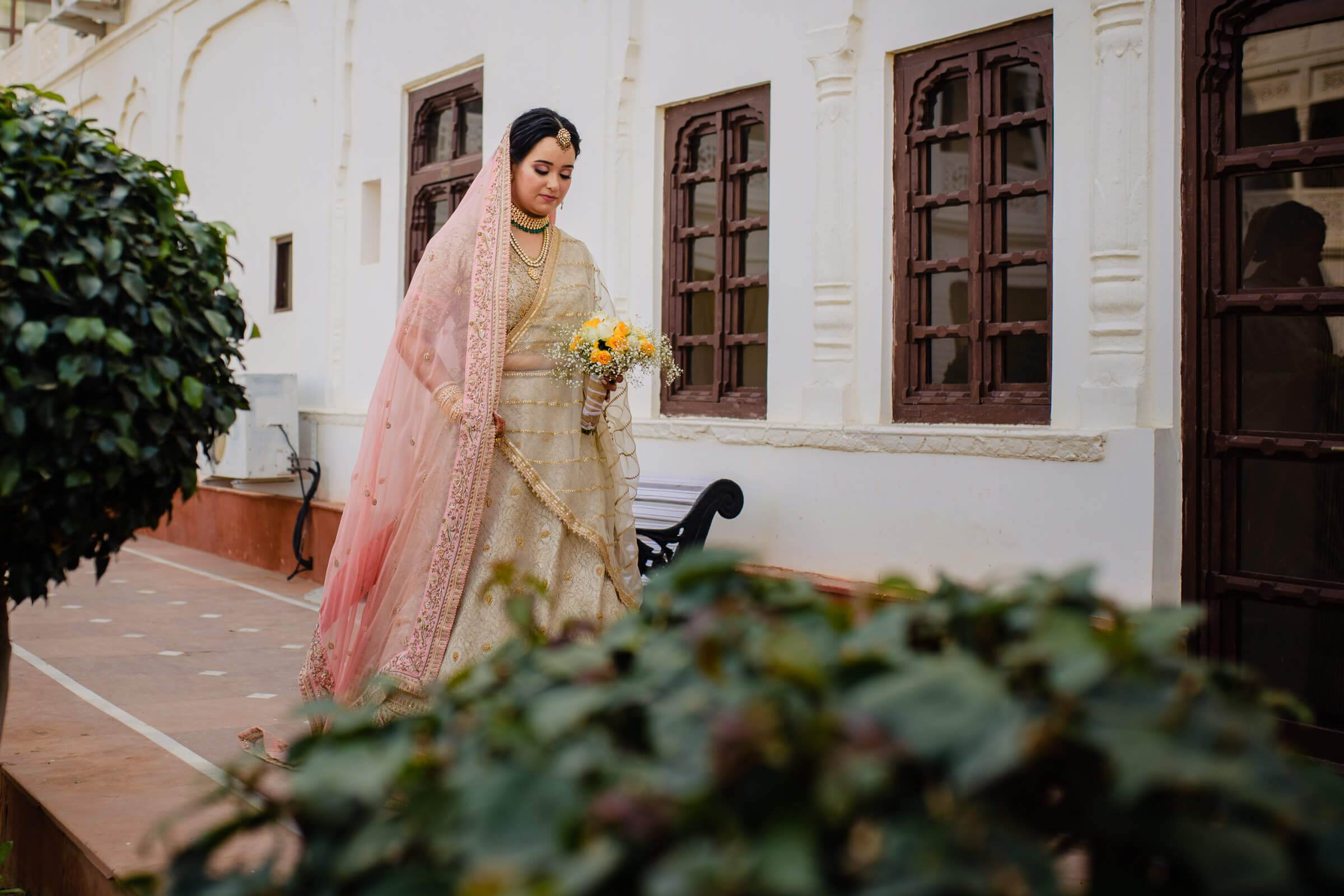 Maitrayee in traditional gold and pink lehenga with yellow flowers, standing in Rajasthan courtyard