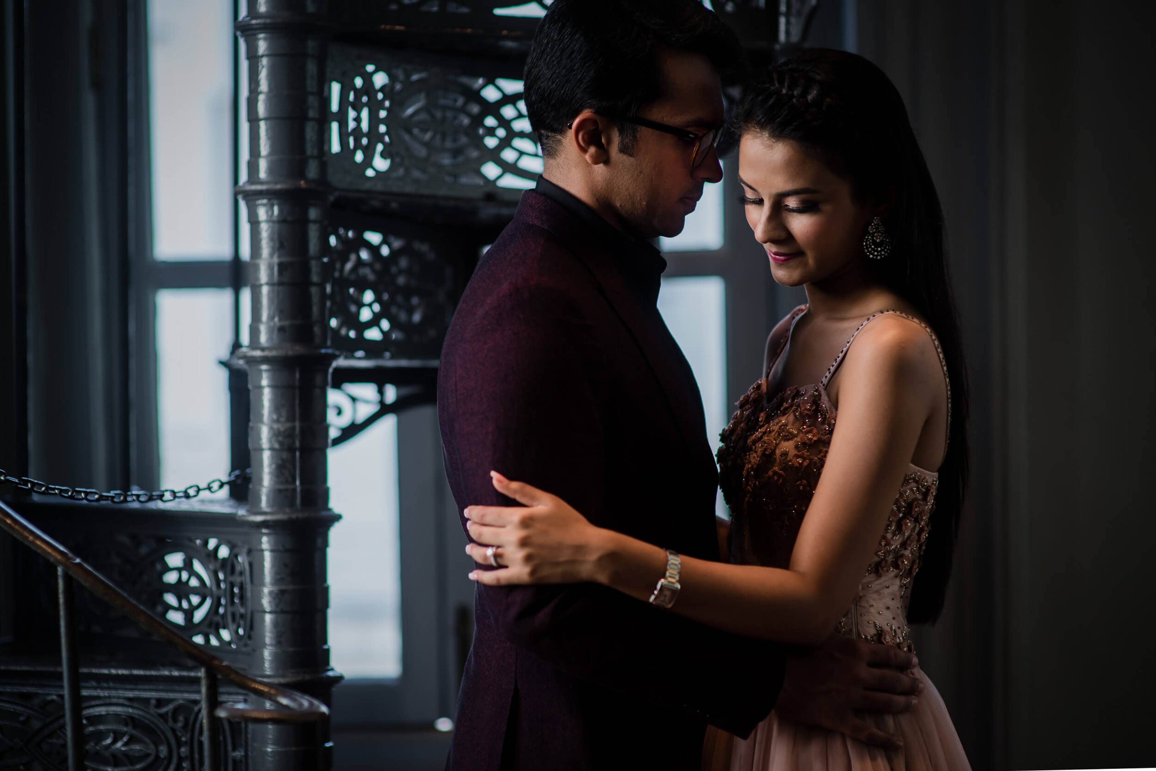Yash and Disha embrace by an ornate window in Singapore, soft light illuminating their intimate moment